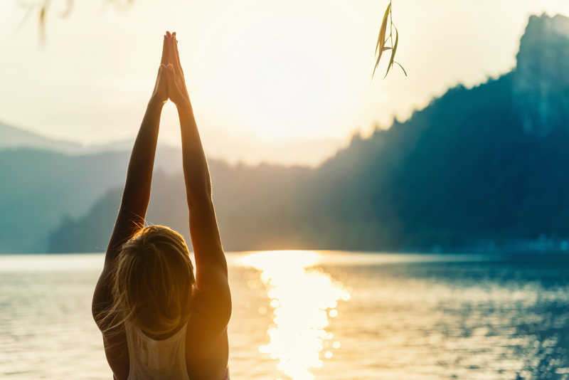 美丽的女人向上的手姿在湖边练瑜伽