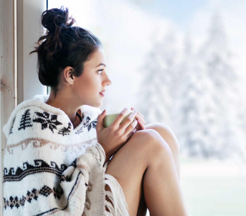 冬日坐在窗边喝咖啡的年轻漂亮女孩