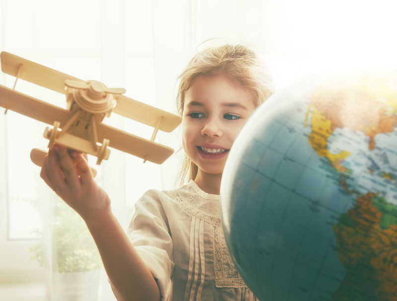 地球仪旁的孩子手拿木制飞机