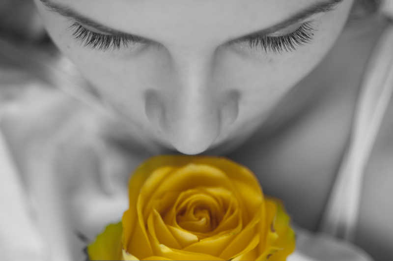 用手捧着黄色玫瑰花闻着花香的女人