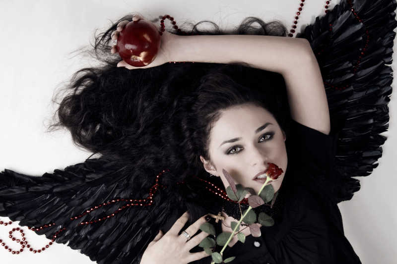 手里拿着玫瑰花与苹果的美女躺在翅膀背景上