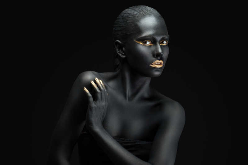 黑色背景上全身漆黑的女人指尖和嘴唇涂着金粉