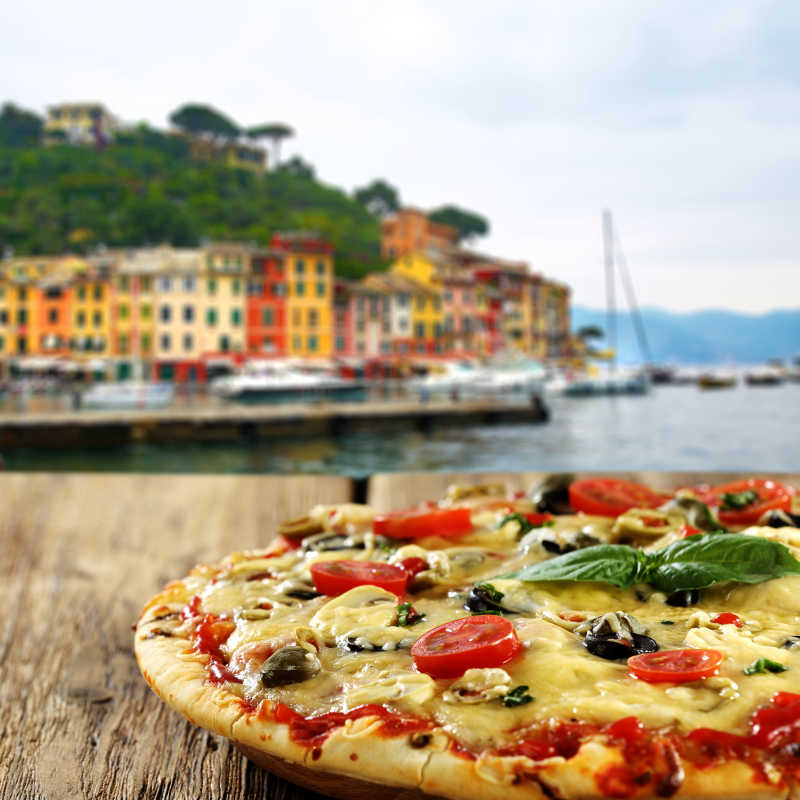 海边小镇模糊背景下木桌上的番茄披萨特写