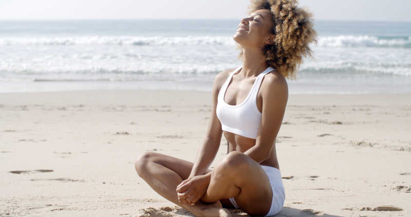 坐在海滩上瑜伽姿势抬头微笑的卷发女人