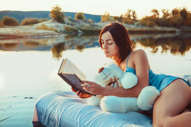 年轻的女孩躺在漂浮的床上看书