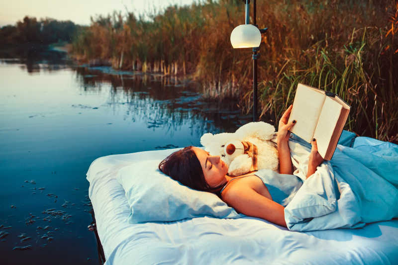 女孩手里拿着一本书舒服的躺在漂浮床上