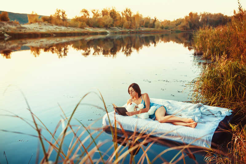 在湖面的漂浮床上看书的年轻女孩
