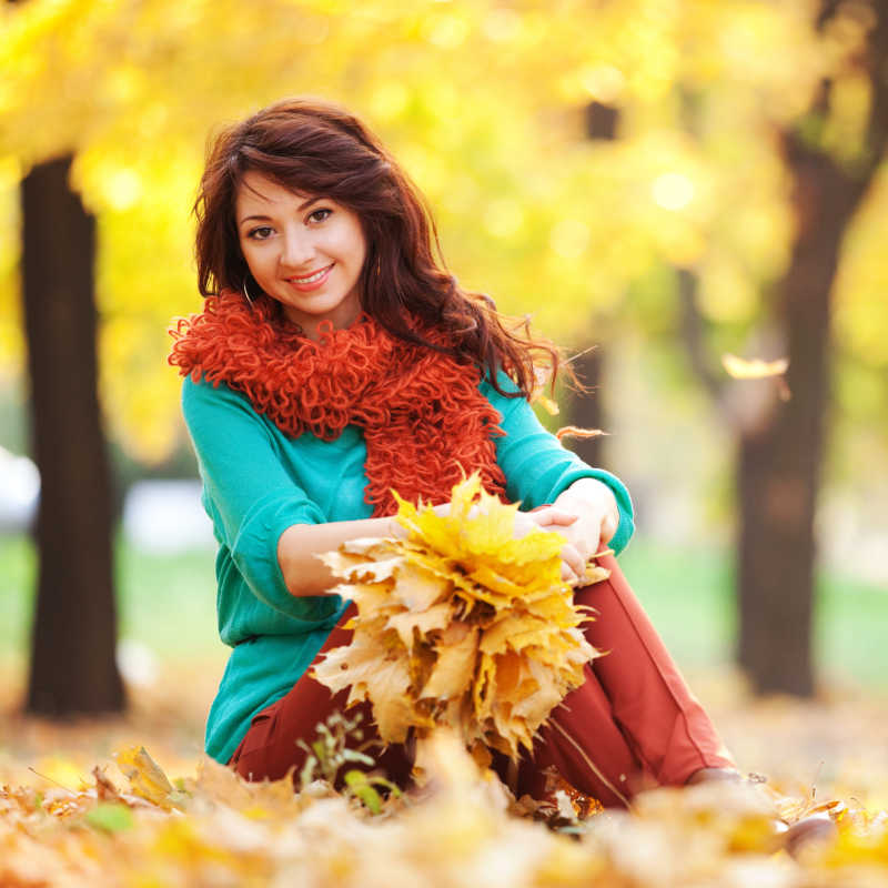 秋天公园里的年轻美女拿着树叶在微笑