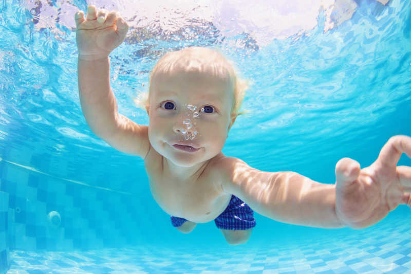 滑稽的小男孩在水中游泳和潜水的照片