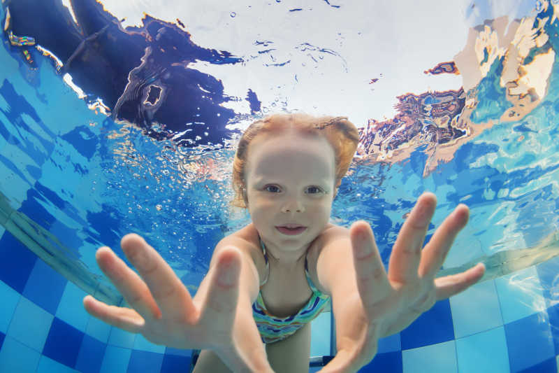 滑稽的小女孩在水中游泳和潜水的照片