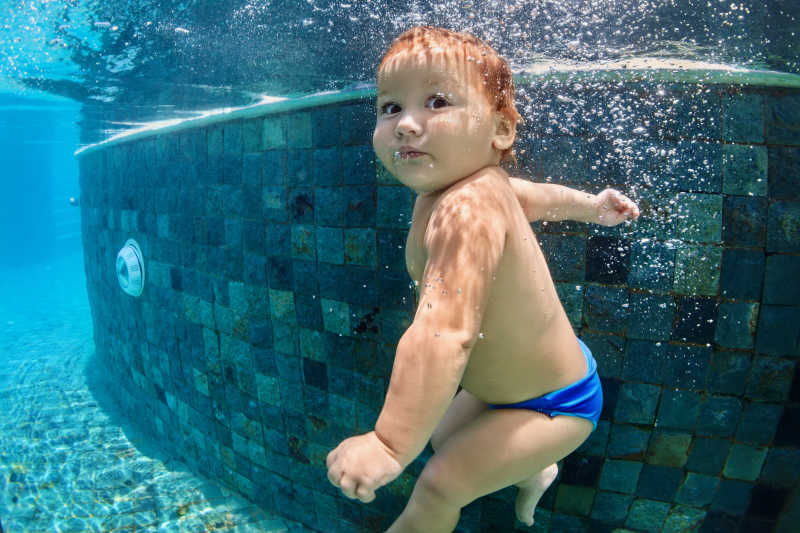 活泼的婴儿游泳和跳水在游泳池与乐趣