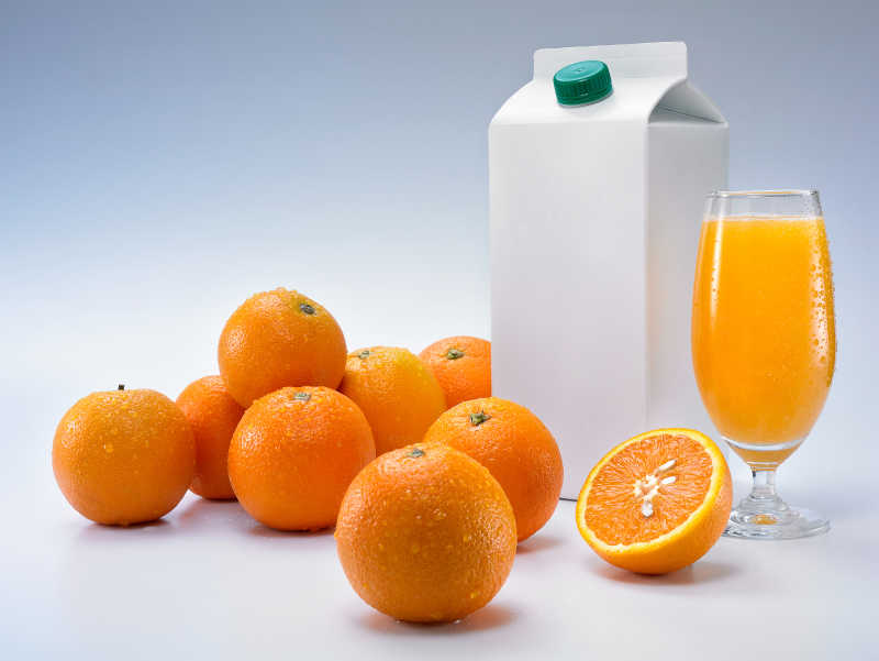 灰色背景下的橙子和一杯橙汁