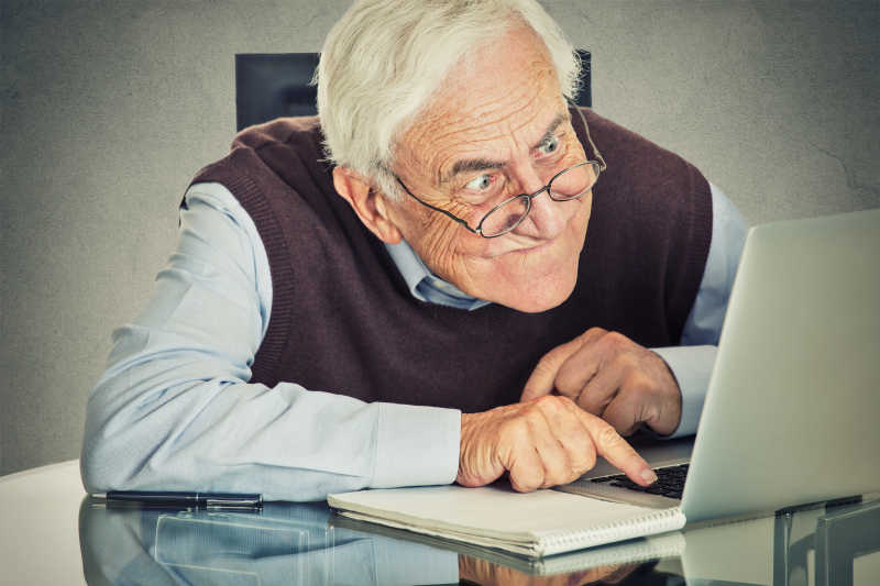 老人坐在桌旁使用笔记本电脑