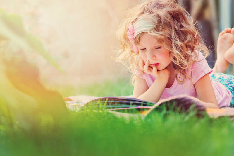 小女孩趴在草地上看书