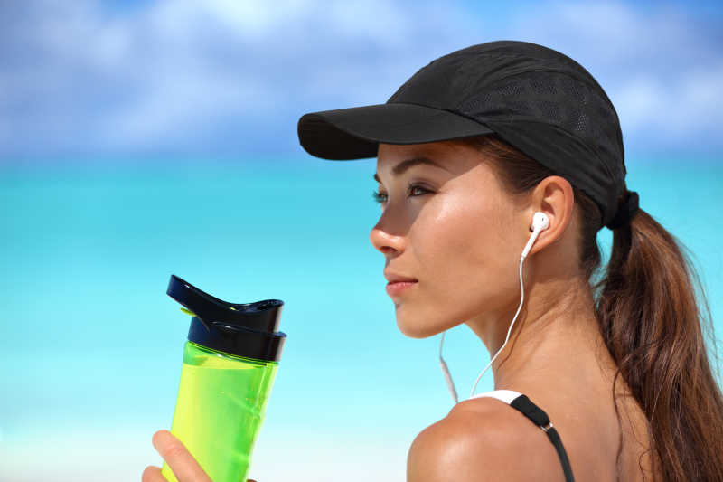 海滩上戴着耳机拿着水杯的女孩