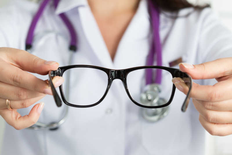 女性眼科医生双手给病人戴上一副黑色眼镜