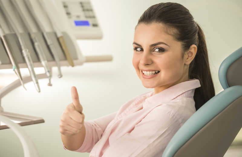 在牙科检查牙齿的美女患者竖起大拇指微笑