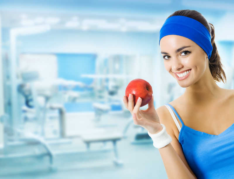 拿着红色苹果在健身房内微笑的女人
