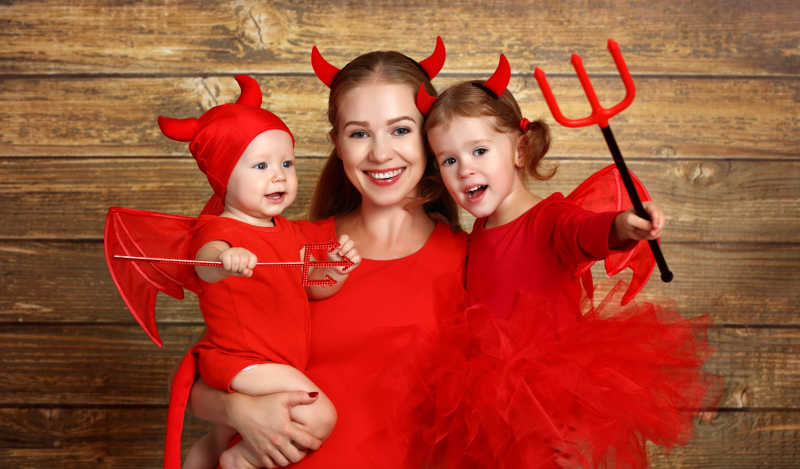 木制背景前快乐的母亲和孩子作恶魔装扮