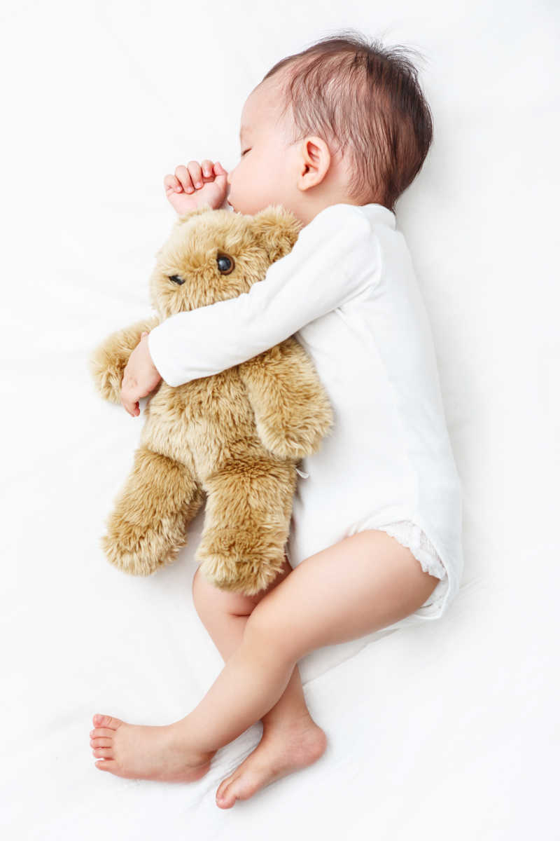 床上可爱的睡着的宝宝和怀里的泰迪熊