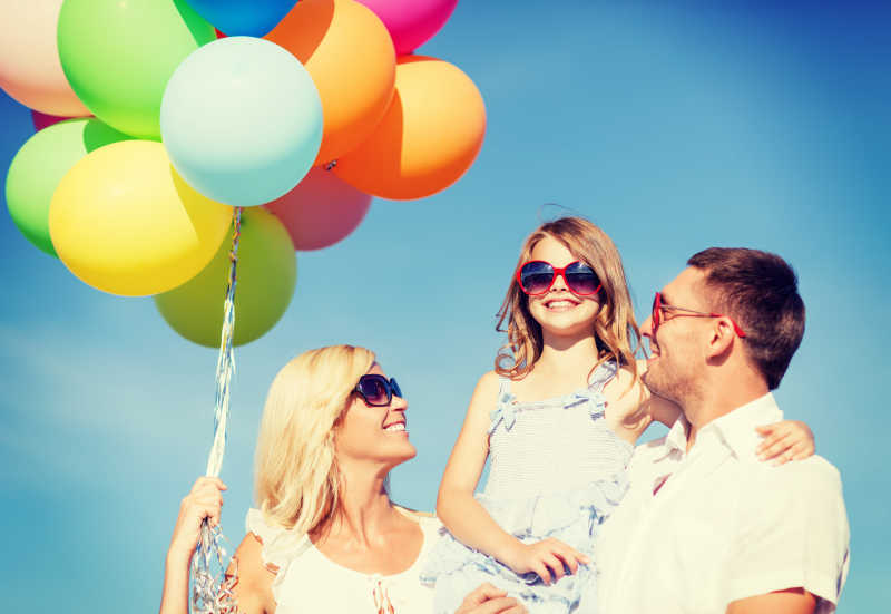 幸福快乐的一家手拿彩色气球在户外度假