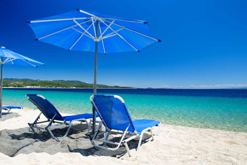 海滩上遮阳伞下的两个蓝色躺椅
