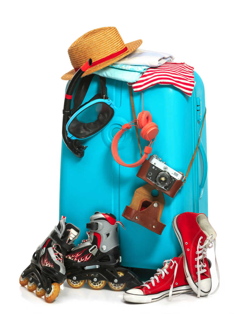 白色背景下放着运动鞋帽子照相机等外出旅行物品的旅行箱
