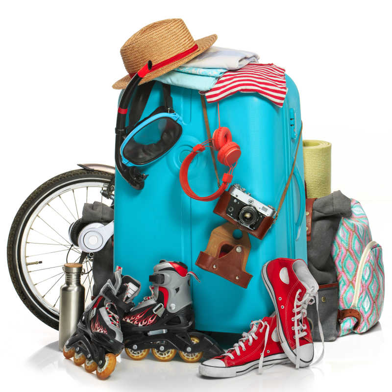 白色背景下放着滑板鞋运动鞋照相机自行车等外出物品的蓝色旅行箱