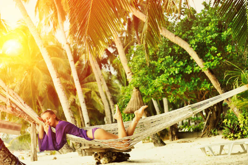 穿紫色衣服趴在沙滩吊床上的美女