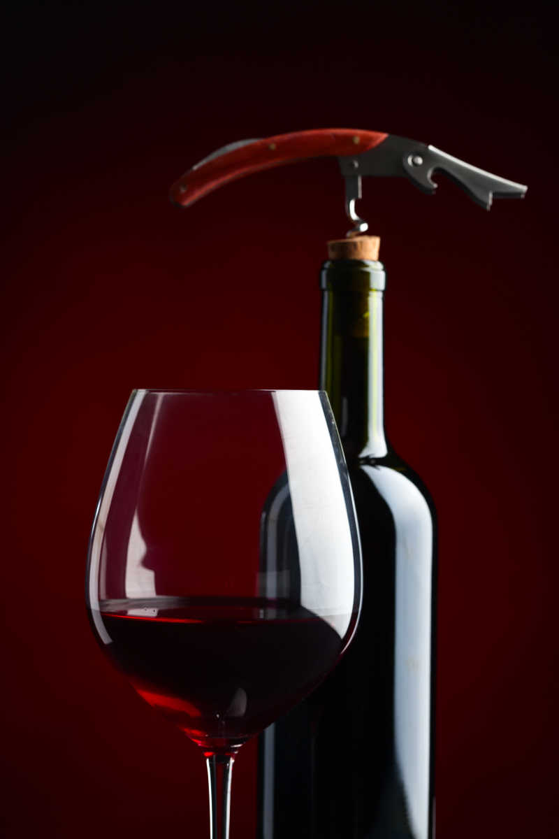红色背景上的红酒杯和红酒瓶上的开瓶器