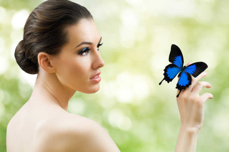 自然背景上的年轻女人和她手上的蝴蝶