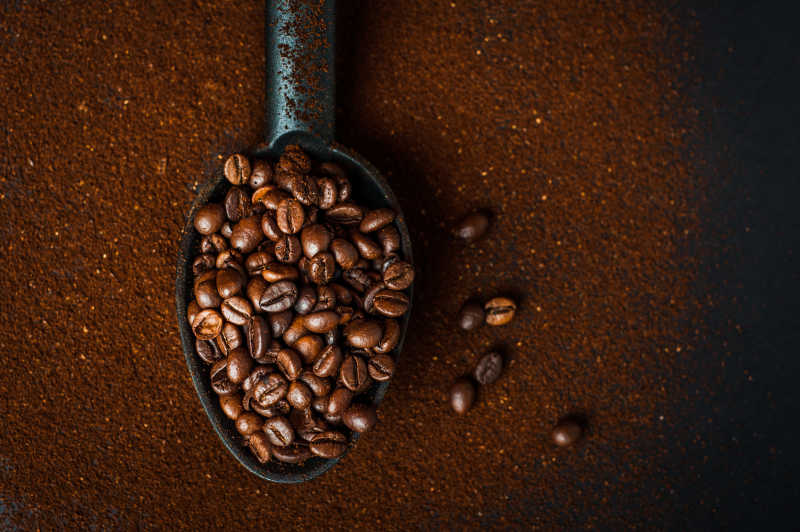 咖啡粉背景上的一勺子咖啡豆