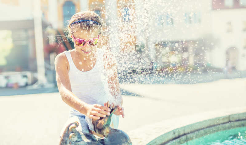 炎热的天气户外可爱的小女孩玩喷泉