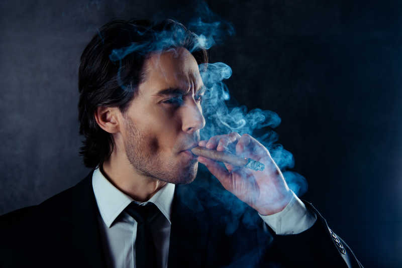 残暴的英俊男子用烟茬抽雪茄的肖像