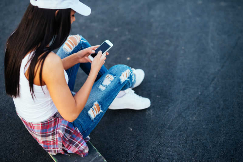 女孩坐在滑板上使用手机