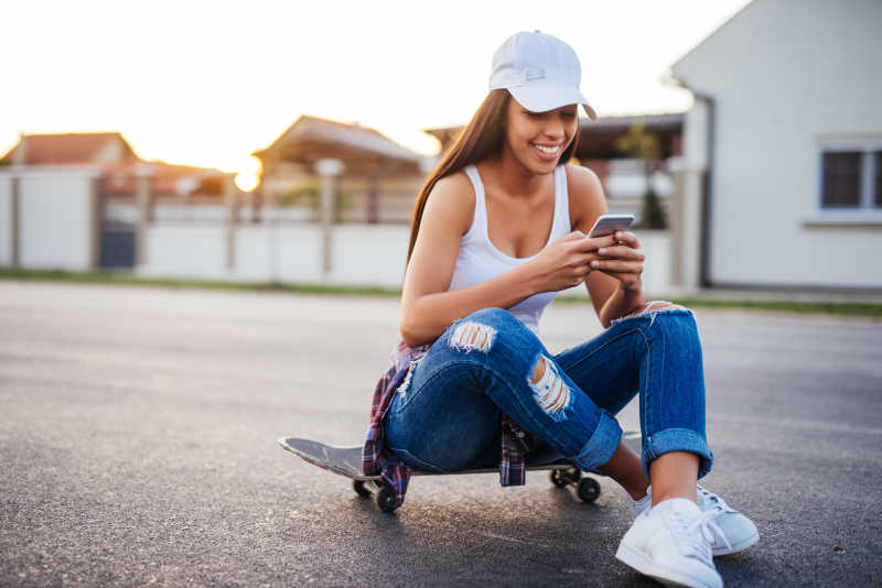 年轻女孩坐在滑板上玩手机