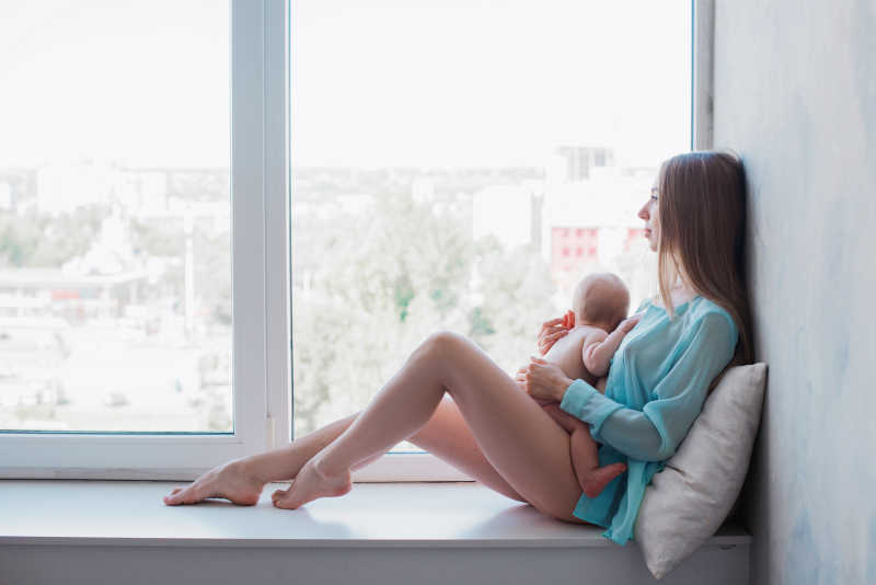 怀抱小婴儿坐在飘窗台的年轻母亲