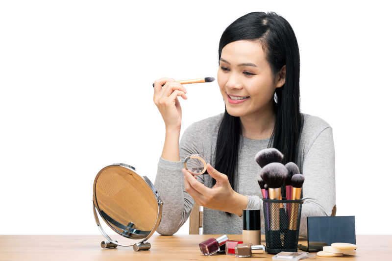 白色背景下拿着工具化妆的亚洲美女