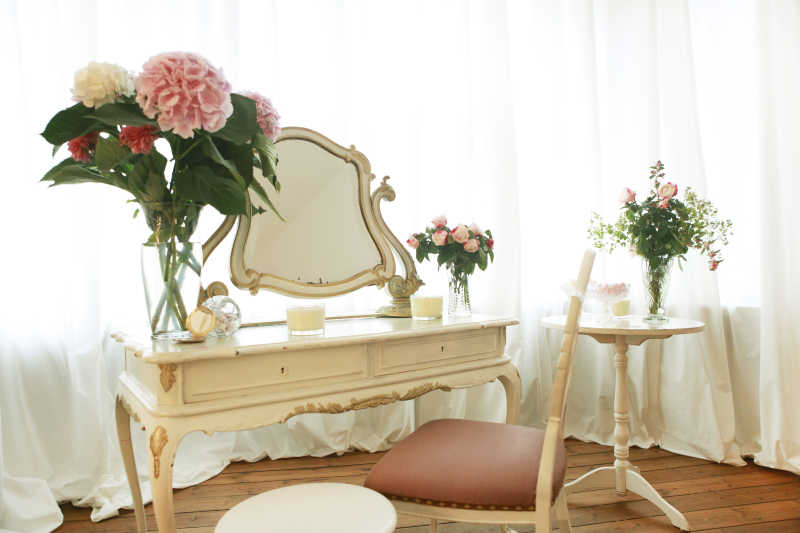 白色有纱帘的木地板上的有花朵和化妆镜的化妆台