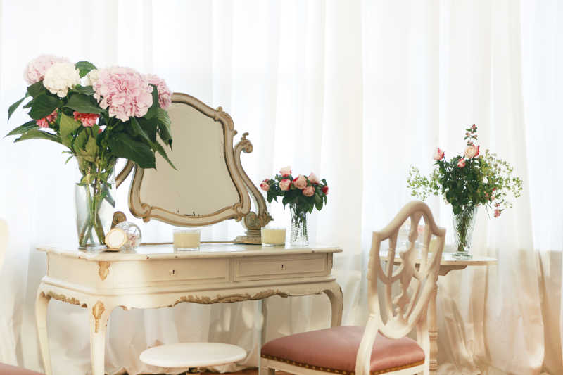 白色有纱帘的室内有花朵和镜子的化妆台