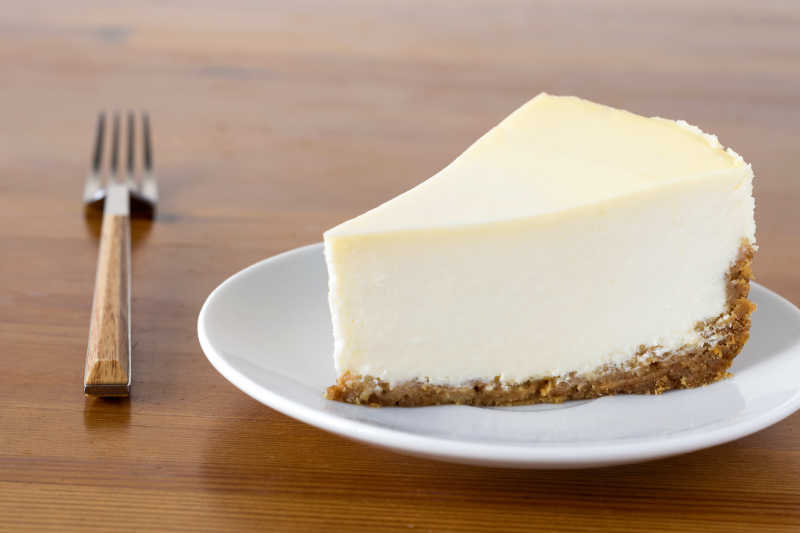 一块纯纽约芝士蛋糕在木板上的白色盘子上