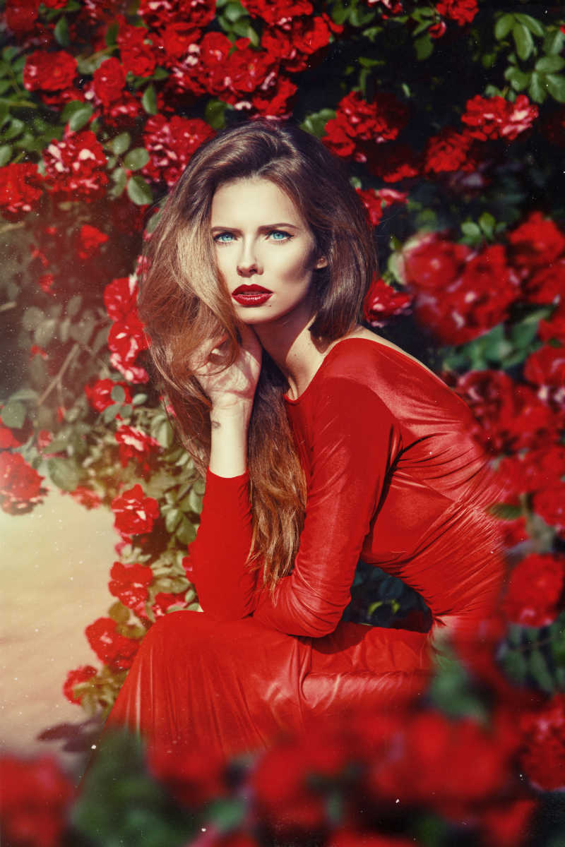 身穿红色衣服的美丽的女人在充满玫瑰的花园里