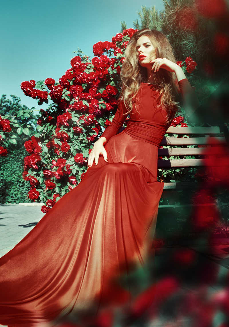 花园里装满玫瑰花的穿着红衣服的美丽的美女