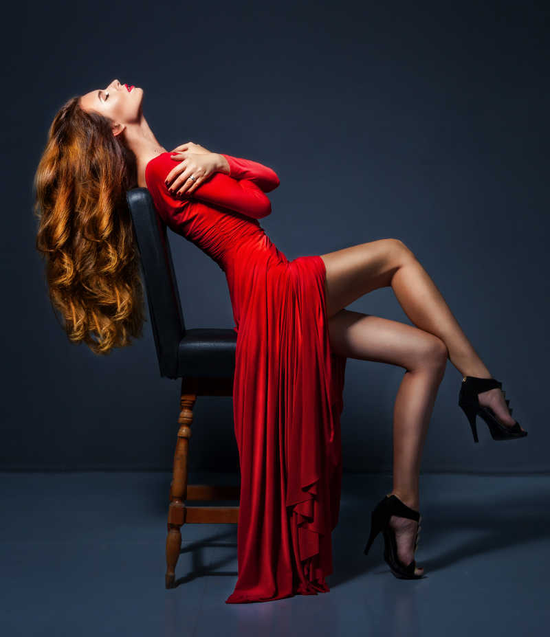 穿着红色长裙坐在椅子上的迷人的女人