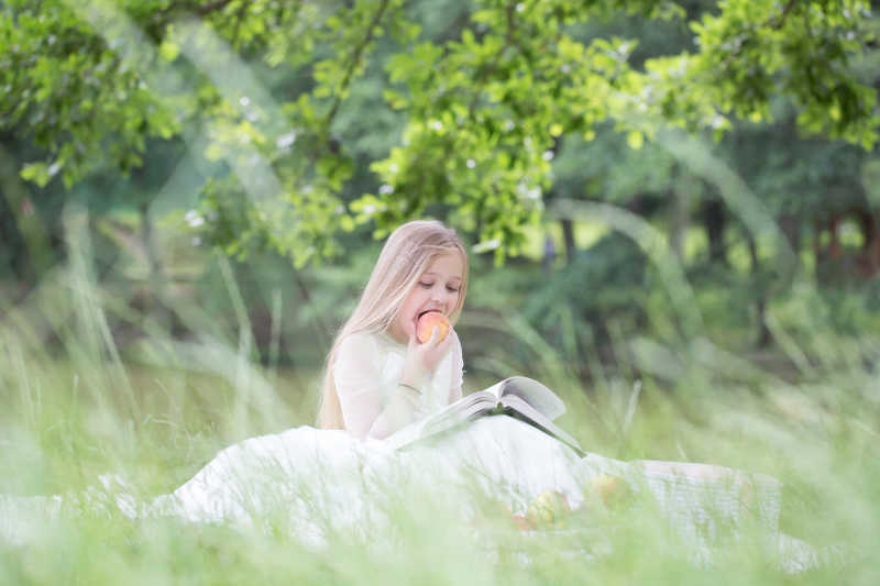 坐在草地上看书吃着苹果的小女孩