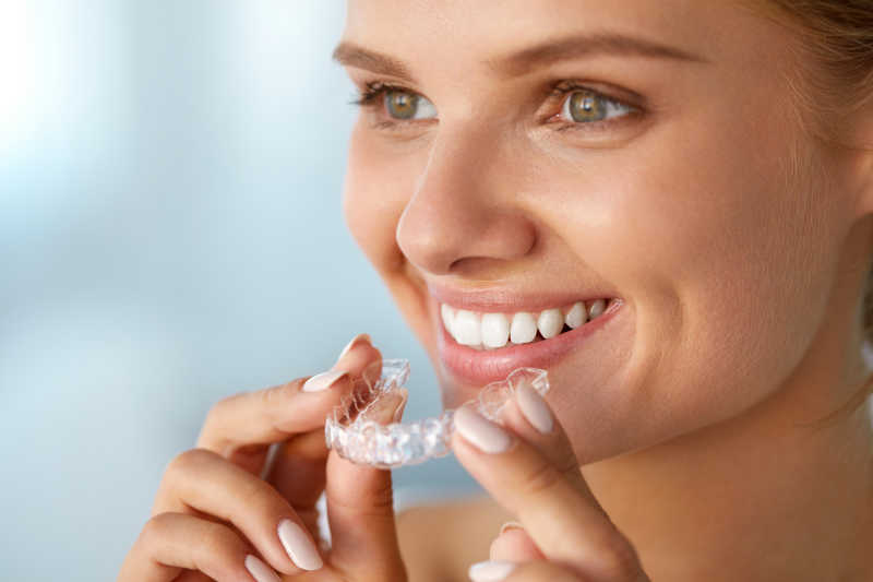 微笑的女人用白色牙齿托着牙齿美白托盘