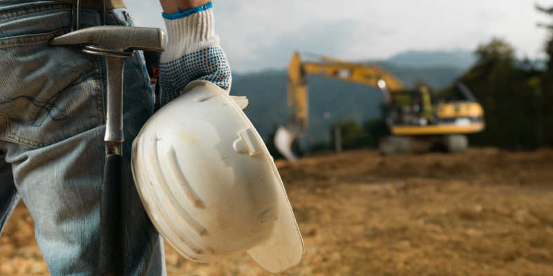 站在工地上的男工程师拿着白色安全帽勘察现场