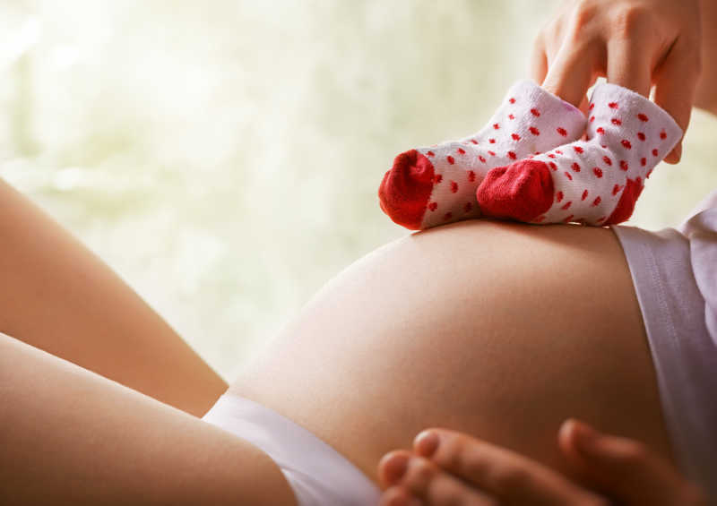 大肚子的孕妇将小孩袜子放在自己的肚子上