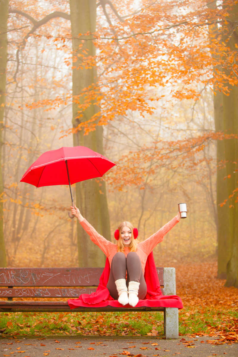 秋天公园里的女孩拿着伞享受热饮