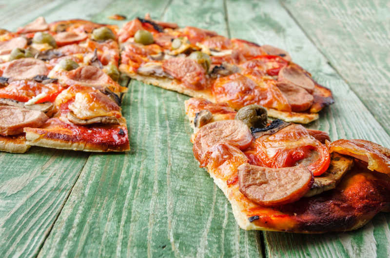 绿色木桌上切成块的烤肉披萨
